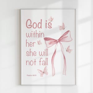 Pode incluir: Impressão emoldurada com fundo branco com o texto rosa "God is within her she will not fall". Um laço rosa e várias borboletas rosas também são retratados. O texto "Psalm 46:5" está na parte inferior.