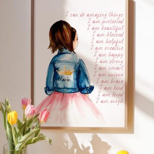 Könnte beinhalten: Ein gerahmter Kunstdruck mit einer Aquarellillustration eines Kindes von hinten, das eine blaue Jeansjacke mit einer goldenen Krone und dem Namen Marin über einem rosa Rock trägt. Der Text lautet: I can do amazing things, I am protected, I am beautiful, I am blessed, I am helpful, I am creative, I am happy, I am strong, I am smart, I am unique, I am brave, I am kind, I am loved, I am enough.
