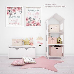 May include: Two framed watercolor prints with pink roses and inspirational quotes. The prints are hung on a white wall above a white shelf with pink and white storage boxes. The shelf is part of a white dollhouse-style bookcase.