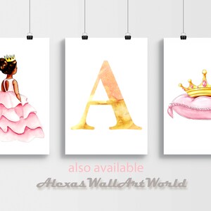 May include: Three framed watercolor prints. The left print features a princess in a pink dress and a gold crown. The center print displays a gold letter "A". The right print shows a gold crown on a pink pillow.