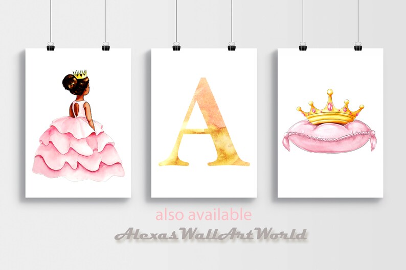 May include: Three framed watercolor prints. The left print features a princess in a pink dress and a gold crown. The center print displays a gold letter "A". The right print shows a gold crown on a pink pillow.