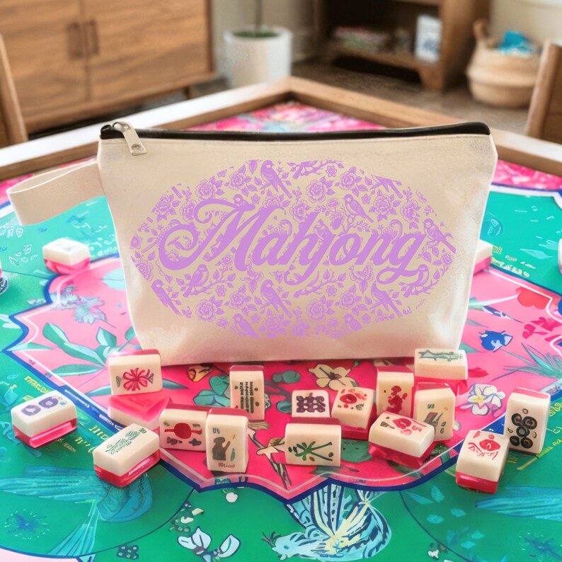 May include: A beige canvas Mahjong bag with a black zipper and handle, featuring a purple floral lip design with the word "Mahjong". The bag is surrounded by Mahjong tiles on a colorful game board.