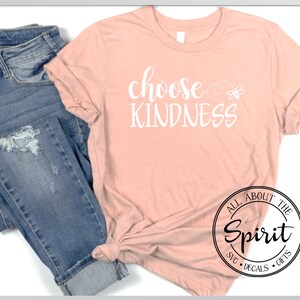 Pu&ograve; includere: Una maglietta color pesca con il testo "choose kindness" in lettere bianche. La maglietta &egrave; abbinata a un jeans blu. L'immagine include anche un logo in bianco e nero che dice "All About The Spirit SVG Decals Gifts".