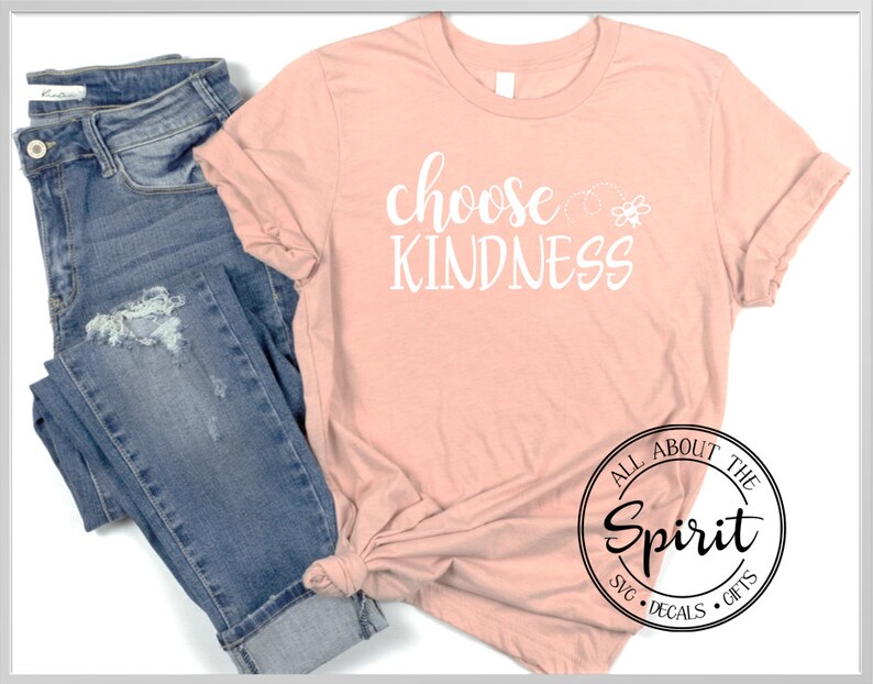 Pu&ograve; includere: Una maglietta color pesca con il testo "choose kindness" in lettere bianche. La maglietta &egrave; abbinata a un jeans blu. L'immagine include anche un logo in bianco e nero che dice "All About The Spirit SVG Decals Gifts".