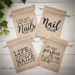 May include: Four beige burlap drawstring bags with black text. The bags have different phrases: "Life isn't perfect but your nails can be", "Nail Stash", "Life is too short to wait for your nails to dry", and "Life isn't perfect but your nails can be".