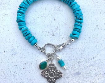 May include: Turquoise gemstone bracelet with a silver charm featuring a decorative design and a smaller turquoise stone. The bracelet also has a green gemstone charm.