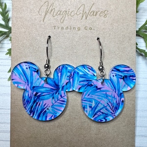 May include: A pair of blue and pink tropical leaf print Mickey Mouse shaped earrings with silver hooks. Magic Wares Trading Co. is printed on the card.