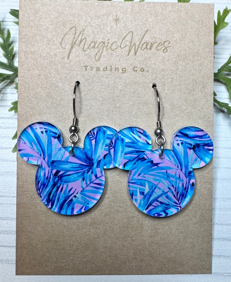 May include: A pair of blue and pink tropical leaf print Mickey Mouse shaped earrings with silver hooks. Magic Wares Trading Co. is printed on the card.
