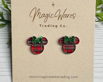 May include: A pair of red and black plaid mouse-shaped earrings with green glitter bows. The earrings are displayed on a tan card with the text "Magic Wares Trading Co." and the website address www.magicwarestrading.com.