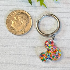 May include: A silver hoop earring with a colourful confetti Mickey Mouse charm. The charm is about the size of a ten pence piece.