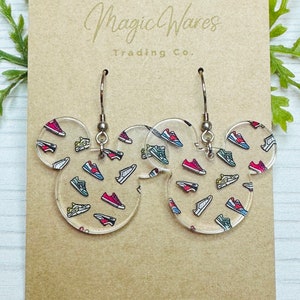 May include: A pair of clear acrylic earrings with a Mickey Mouse shape. The earrings are decorated with a pattern of colorful sneakers.