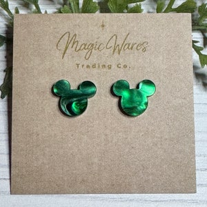May include: A pair of green and black Mickey Mouse-shaped earrings. The earrings are made of a marbled material with a glossy finish.