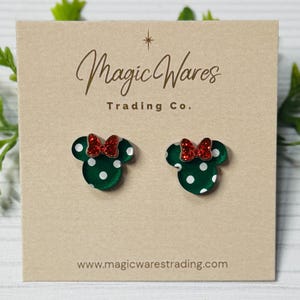 May include: A pair of green and white polka dot mouse-shaped earrings with red bows. The earrings are displayed on a tan card with the text "Magic Wares Trading Co." and the website address.