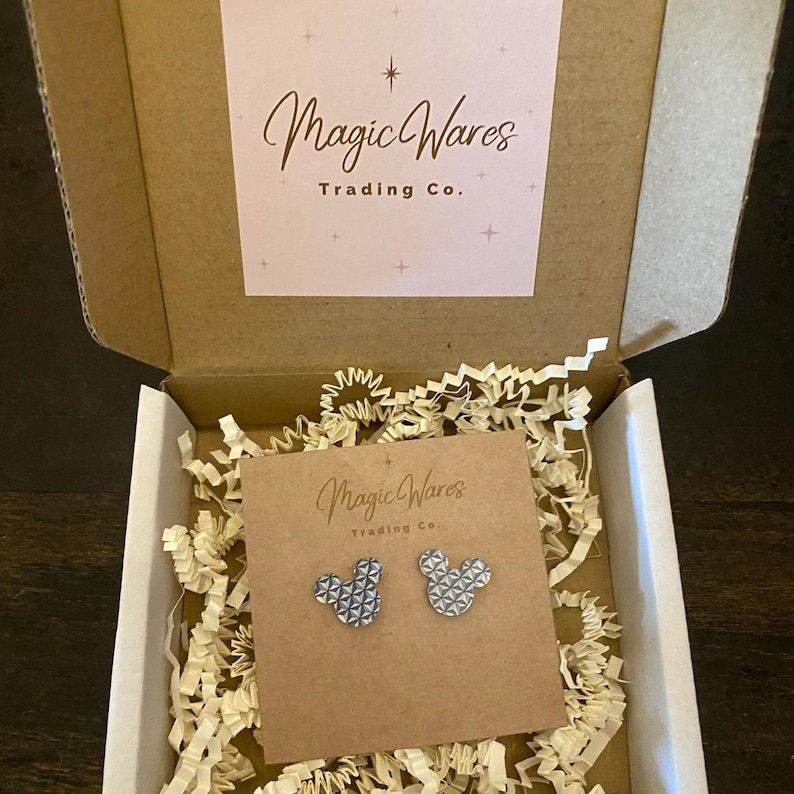 May include: A pair of silver Mickey Mouse earrings with a geometric pattern, packaged in a small box with a Magic Wares Trading Co. label.