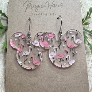 May include: Clear acrylic earrings shaped like Mickey Mouse ears with a pink flamingo pattern. The earrings have silver hooks.