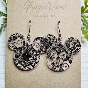 May include: A pair of black and white damask print Mickey Mouse earrings with silver hooks. The earrings are on a brown card with the text "Magic Wares Trading Co."