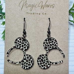 May include: A pair of dangle earrings with a black and white leopard print design. The earrings are shaped like Mickey Mouse ears.