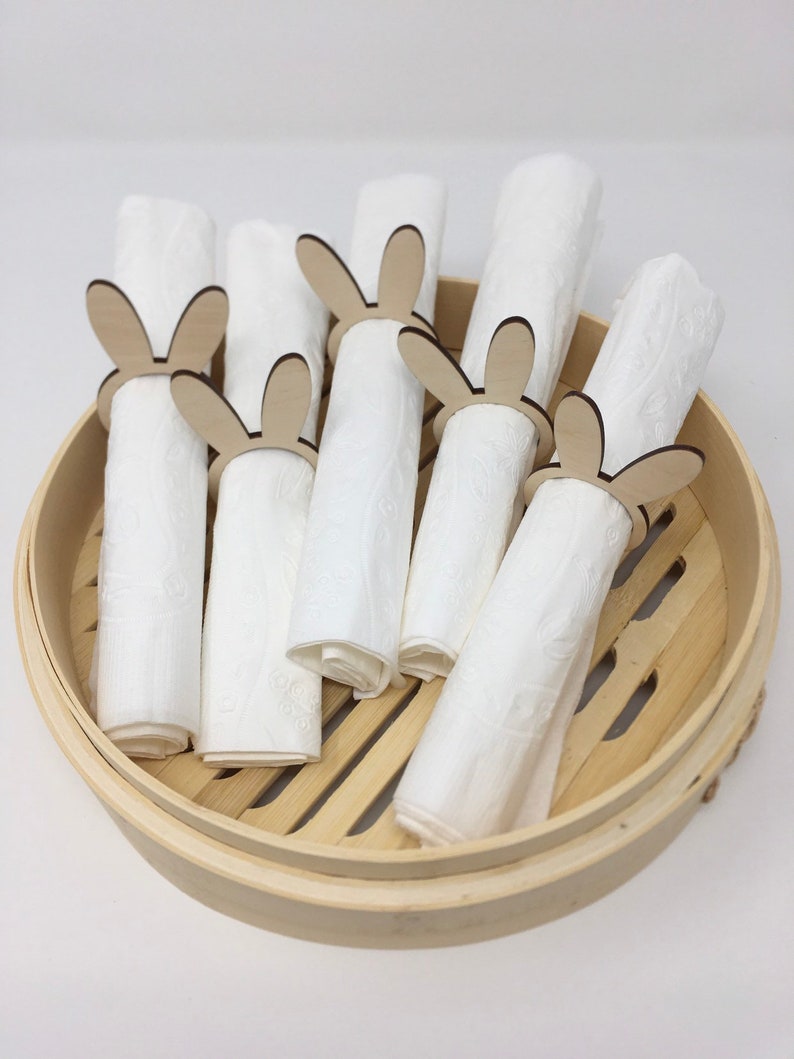 Puede incluir: Un juego de seis servilletas blancas con anillos de servilleta de madera con forma de conejo. Los anillos son de madera natural y tienen un dise&ntilde;o de conejo simple. Las servilletas y los anillos est&aacute;n en un vaporizador de bamb&uacute; redondo.