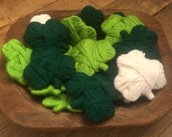 May include: A wooden bowl filled with handmade shamrocks in shades of green and white. The shamrocks are made of yarn and are arranged in a rustic wooden bowl, perfect for St. Patrick's Day decorations.