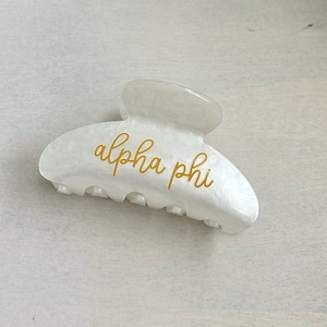 May include: White plastic hair claw with gold lettering that says "alpha phi".