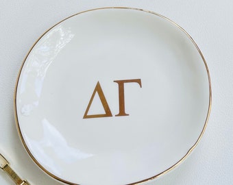 May include: White ceramic trinket dish with a gold rim and the letters "ΔΓ" in gold lettering.
