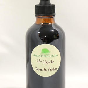 以下が含まれることがあります： 黒いスポイトトップが付いた、濃い茶色のガラス瓶。ボトルには「Green Heron Acres 4-Herb Parasite Combo」と書かれた丸いラベルが付いています。ボトル内の液体は濃い色です。