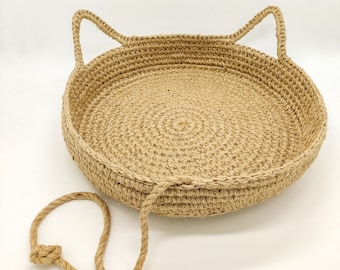 Pode incluir: Uma cama redonda para gatos em juta tecida, com alças em forma de orelhas. A cama de cor bege natural tem um detalhe de corda e é projetada para animais de estimação. Aproximadamente 40 cm de diâmetro.