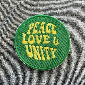 Könnte beinhalten: Ein grüner runder Patch mit gelbem gesticktem Text, der "Peace Love & Unity" lautet.