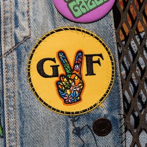 May include: A yellow circle patch with a peace sign and the letters "GVF" in black.