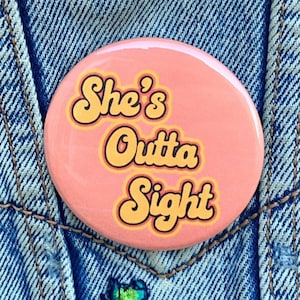May include: A pink button with the text "She's Outta Sight" in yellow retro font.