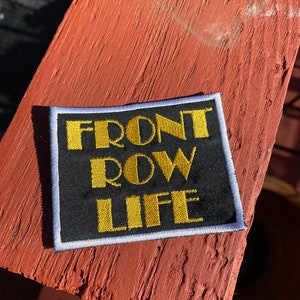 May include: Black embroidered patch with white border. The text "FRONT ROW LIFE" is embroidered in yellow.