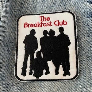 May include: White patch with red embroidered text "The Breakfast Club" and black silhouettes of five people standing together.