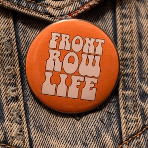 May include: Orange button with white text that reads "FRONT ROW LIFE" in a retro font style.