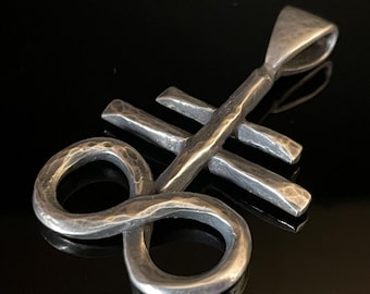 May include: A silver pendant in the shape of a stylized infinity symbol with a crossbar. The pendant has a hammered texture and a loop at the top for attaching a chain.