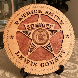 May include: A wooden plaque with a sheriff's star design. The plaque is engraved with the words "Patrick Smith Sheriff Lewis County" and features the Great Seal of the State of New York.