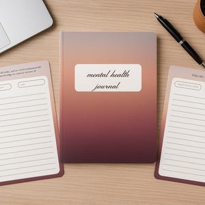 以下が含まれることがあります： グラデーションの表紙に「mental health journal」の文字が入った、メンタルヘルスジャーナル。白い長方形の中にあります。罫線入りのページとプロンプトが付いた2つのメモ帳が両側にあります。ペン、植物、ラップトップも表示されています。
