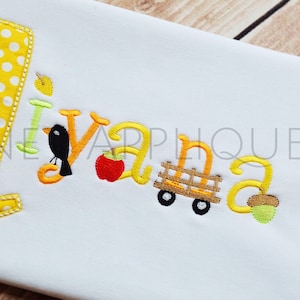 May include: A white onesie with yellow polka dot fabric, embroidered with the number "1", the name "Ivana", a bird, an apple, a wagon, and an acorn.