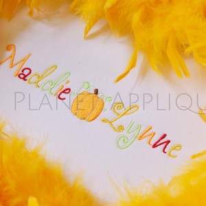 May include: Embroidered design featuring the names Maddie and Lynne with a small pumpkin in between. The names are in a rainbow of colors and the pumpkin is orange with green vines.
