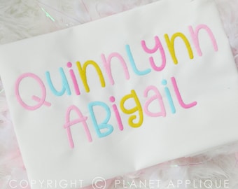 Op de afbeelding: Wit T-shirt met de namen "Quinnlynn" en "Abigail" geborduurd in roze, geel en blauw.