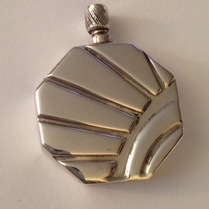 May include: A silver-colored, geometric flask with a textured screw-on cap. The flask has a unique, multi-faceted design with angled lines radiating from the center. The metallic surface reflects light, highlighting its shape and details. A stylish accessory.