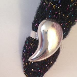 May include: A silver ring with a pointed, curved design. The ring is on a black fabric with colorful threads.