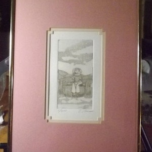 May include: A framed black and white etching of a girl sitting on a fence. The etching is set against a pink background and has a white mat.