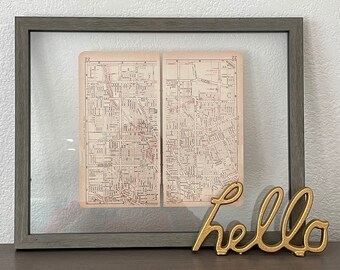 May include: A framed vintage map of a city with a gold metal "hello" sign in the foreground.