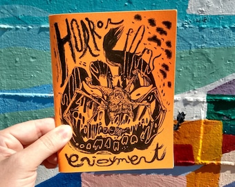 May include: A bright orange booklet with black ink illustrations of a monster with sharp teeth and the words "Horror" and "Enjoyment" on the cover.