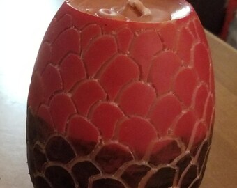 May include: A red and black candle shaped like a dragon egg. The candle has a textured surface that resembles scales.