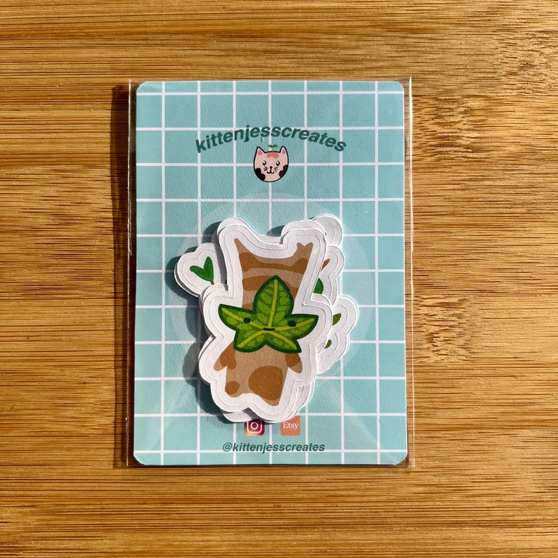 May include: A set of three stickers featuring a cartoon character with a leafy head. The character is brown with a light brown face and green leaves for hair. The stickers are on a blue and white checkered background with the text "kittenjesscreates" and a cat icon.