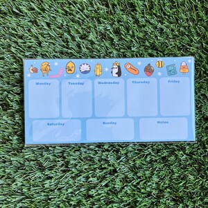 May include: A blue weekly planner with cartoon characters from the show Adventure Time. The planner has spaces for Monday through Sunday and a notes section.