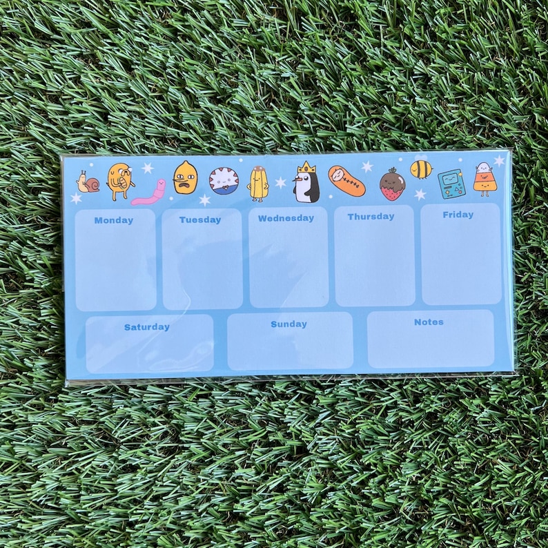 May include: A blue weekly planner with cartoon characters from the show Adventure Time. The planner has spaces for Monday through Sunday and a notes section.