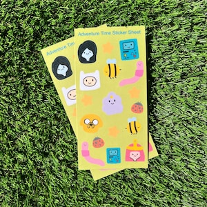May include: A yellow sticker sheet with Adventure Time characters, including Finn, Jake, Princess Bubblegum, and BMO. The sheet also features bees, ladybugs, and stars.