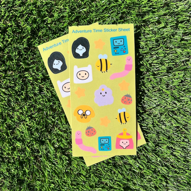 May include: A yellow sticker sheet with Adventure Time characters, including Finn, Jake, Princess Bubblegum, and BMO. The sheet also features bees, ladybugs, and stars.